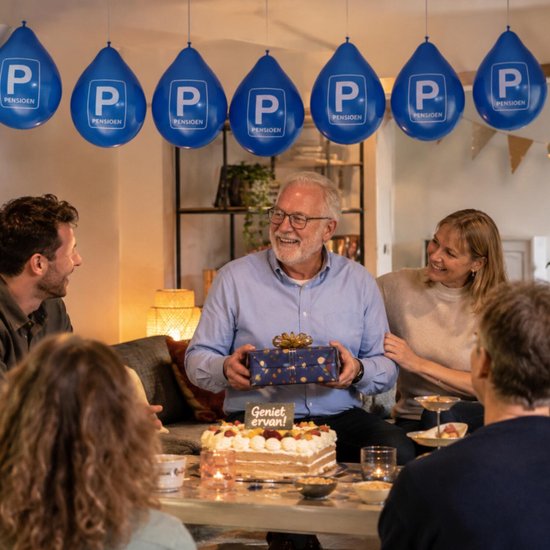 Man ontvangt cadeau tijdens pensioenfeest omringd door familie onder blauwe 'P Pensioen' ballonnen.