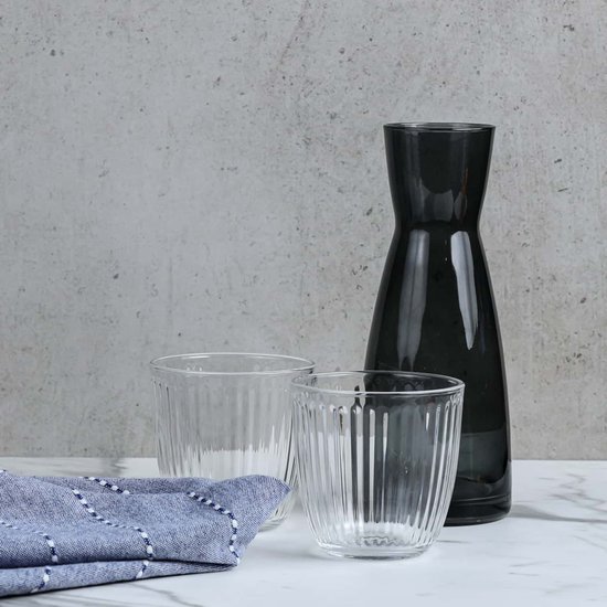 Deux verres à côtes verticales à côté d'une carafe gris foncé. Une serviette bleue rayée est devant.