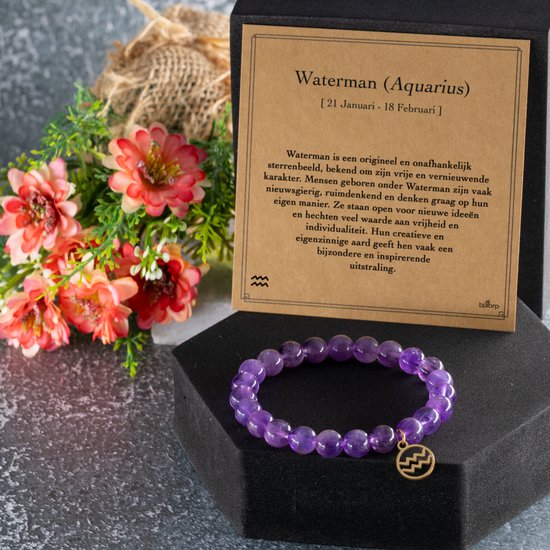Amethist edelsteen armband met gouden Waterman bedel, naast een kaart over Waterman en een boeket bloemen.