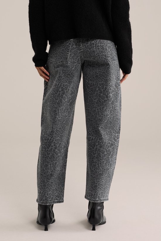 Model van achter met een grijze jeans met luipaardprint en zwarte laarzen.