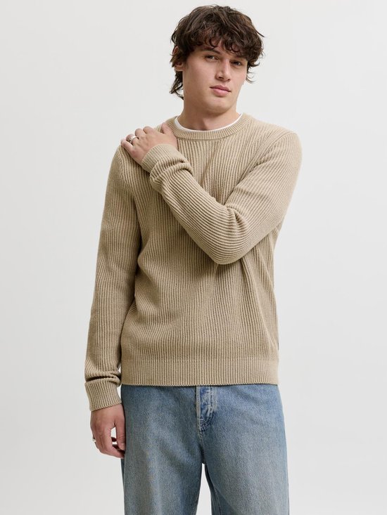Man met beige gebreide trui met ribbels en blauwe jeans, model staat naar voren, hand op de schouder.