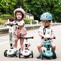 Twee kinderen op Scoot and Ride Highwaykick steps met helmen, een in beige, een in roze en een in groen.