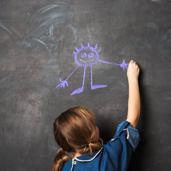 Fille avec des couettes dessinant une figure violette sur un tableau noir avec de la craie.