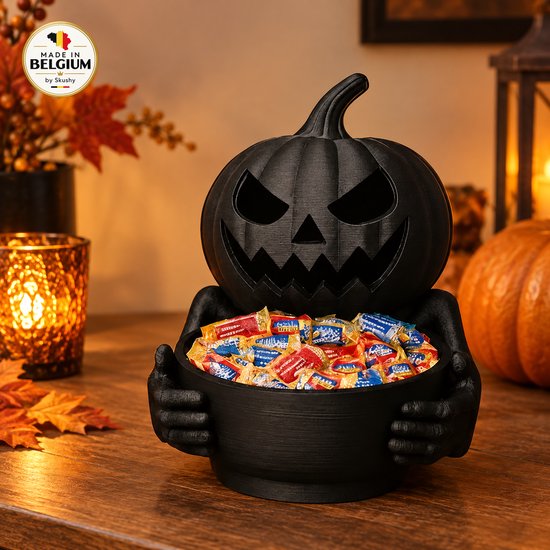 Zwarte pompoenschaal met snoep in een kom, omringd door herfstdecoratie en een kaarslichtje.