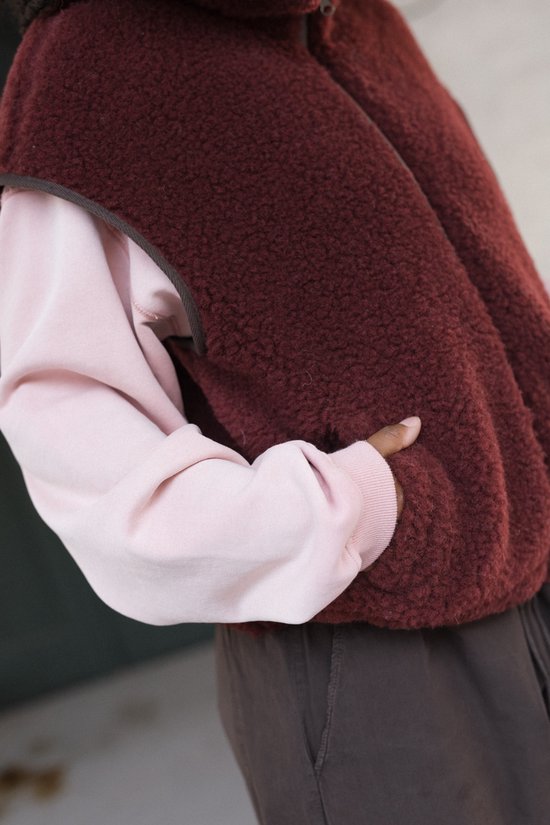 Close-up van de zak van een bordeauxrode wollen bodywarmer gedragen over een roze trui.