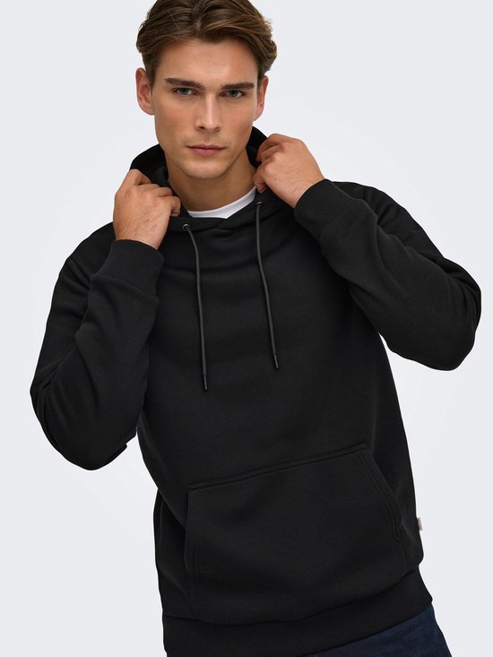 Model houdt de capuchon van een zwarte hoodie vast, zichtbaar met kangoeroezak.