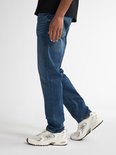 Model draagt een blauwe Petrol Industries jeans met regular tapered fit en witte New Balance sneakers.