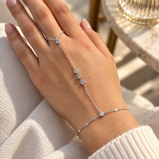 Zilveren handketting met zirkonia's, gedragen door een persoon in een witte gebreide trui.