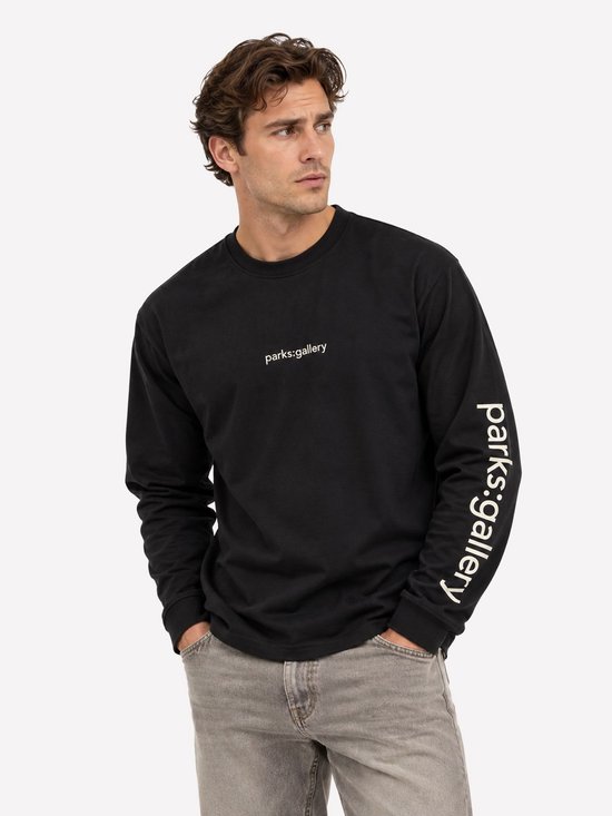 Model draagt een zwart T-shirt met lange mouwen, voorzien van witte 'parks:gallery' tekst op de borst en mouw.
