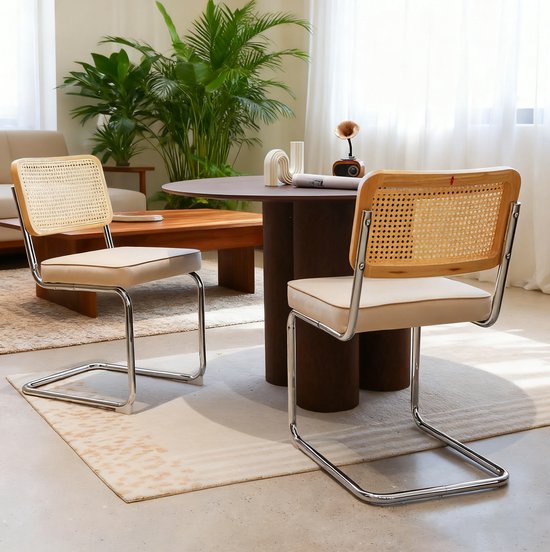 Twee eetkamerstoelen met rotan rugleuning en beige zittingen opgesteld bij een ronde tafel in een lichte woonkamer.