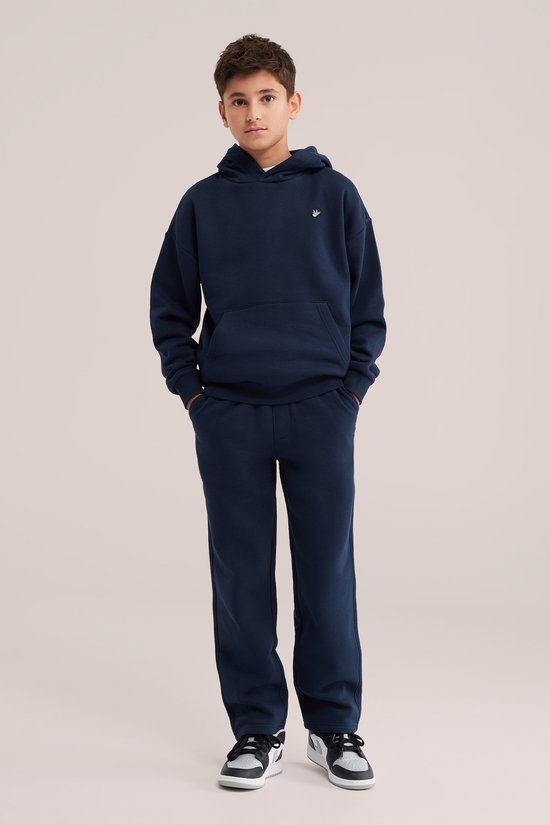 Jongen draagt een donkerblauwe hoodie en bijpassende joggingbroek met een wit vogelborduursel op de borst.