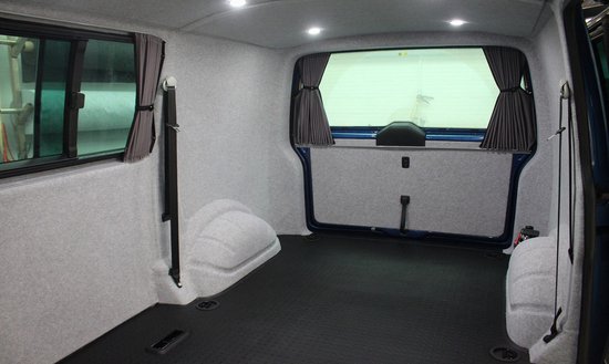 Interieur van een bestelwagen met grijs vloertapijt, grijze wandbekleding en gordijnen.
