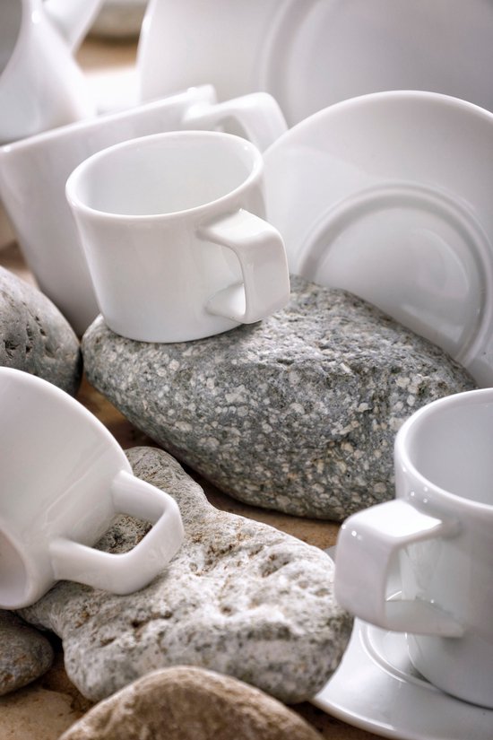 Witte espressokopjes en schotels op grijze en bruine stenen.