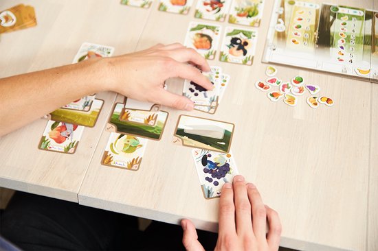Handen die kaarten met afbeeldingen van fruit en dieren in een bordspel leggen op een houten tafel.