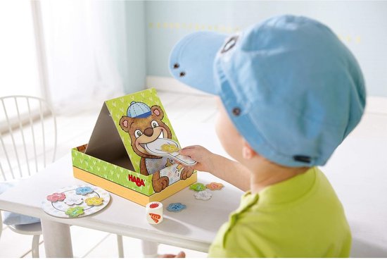 Kind met blauwe pet speelt met HABA Bärnhunger spel: beer met lepel.