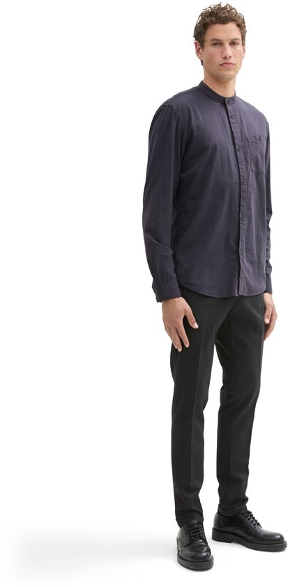 Man met donkerblauw overhemd met opstaande kraag en donkere broek.