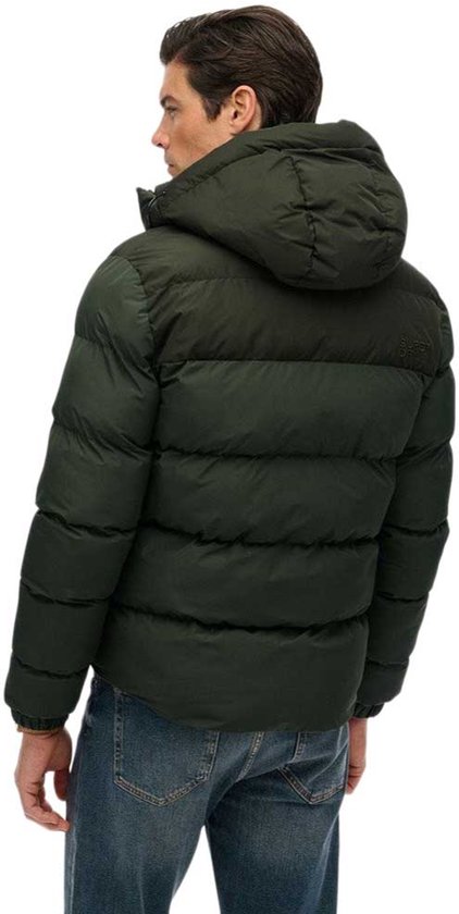 Man, van achteren gezien, in donkergroene, gewatteerde jas met capuchon en jeans.