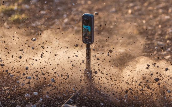 Insta360 X5 action camera midden in een stofwolk van rondvliegende aarde en steentjes.