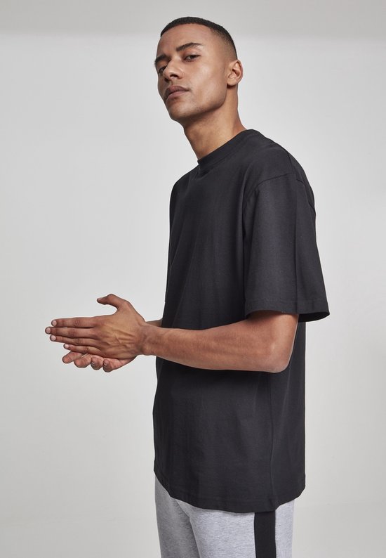 Man in zwart oversized T-shirt en grijze joggingbroek met zwarte streep, handen bij elkaar.