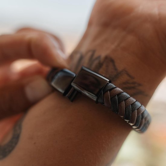 Close-up van een gevlochten bruin-zwarte leren armband met een zwarte magnetische sluiting.