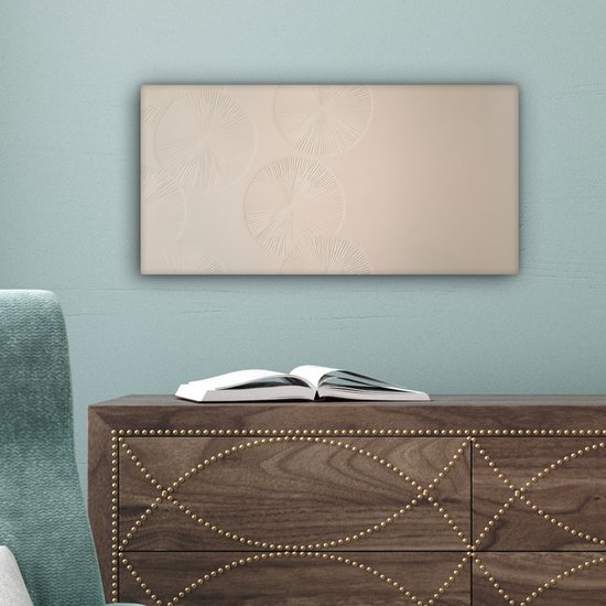 Beige canvas met cirkelvormige patronen, hangend boven een donkerhouten kast met een open boek.