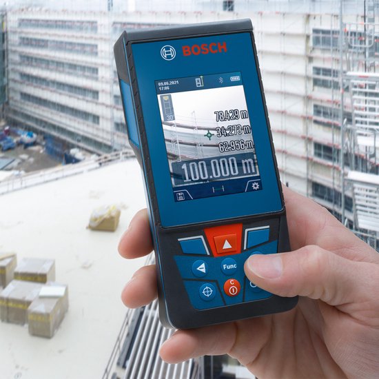 Hand die een Bosch laser afstandsmeter vasthoudt met een bouwplaats op de achtergrond.