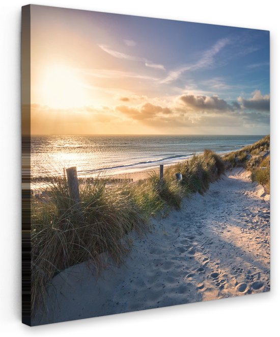Een zandpad met graspollen en houten paaltjes leidt naar een rustige zee tijdens zonsondergang met zonlicht dat door de wolken schijnt.