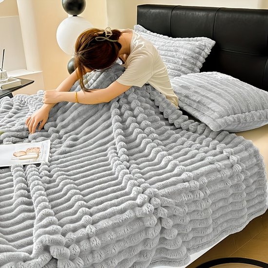 Vrouw op bed onder een grijze geribbelde fleece deken met bijpassende kussens.