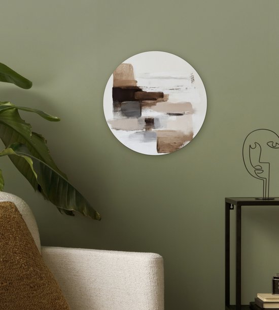 Ronde muurdecoratie met bruine en beige penseelstreken, hangend aan een muur naast een plant.