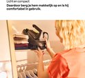 Vrouw met oranje shirt, plaatst een compacte zwarte stoomgenerator met gele accenten in een kast bij de gestapelde kleding.