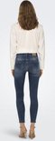 Vrouw van achteren gezien, in een donkerblauwe skinny jeans met rafelige zoom, met beige sandalen.