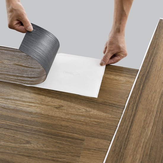 Handen verwijderen de beschermlaag van een zelfklevende laminaatplank met antiek eikenhouten print.
