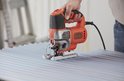 Oranje en zilveren Black+Decker decoupeerzaag, gebruikt op geribbelde metalen plaat.