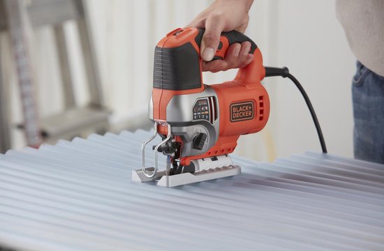 Oranje en zilveren Black+Decker decoupeerzaag, gebruikt op geribbelde metalen plaat.