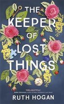 Boekomslag met de titel 'The Keeper of Lost Things' van Ruth Hogan, versierd met roze bloemen, groene bladeren, een sleutel en een puzzelstukje.