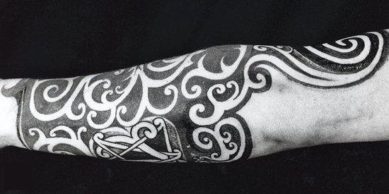 Arm bedekt met een grote, gedetailleerde zwarte tatoeage van golvende lijnen en geometrische patronen.