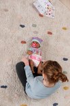 Meisje zit op de grond met babypop op schoot. Pop draagt muts, romper en luier.