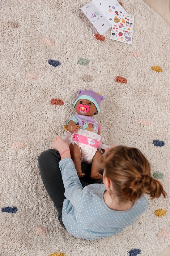 Meisje zit op de grond met babypop op schoot. Pop draagt muts, romper en luier.