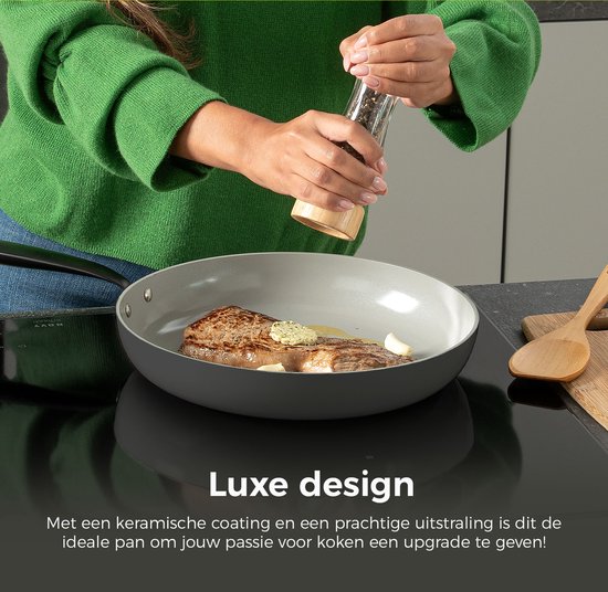 Grijze koekenpan met zwarte steel, met een stuk vlees en knoflook erin. Een vrouw voegt peper toe met een pepermolen. "Luxe design" is zichtbaar.