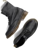Paire de bottes Dr. Martens noires à lacets disposées de manière ludique, avec surpiqûre jaune.