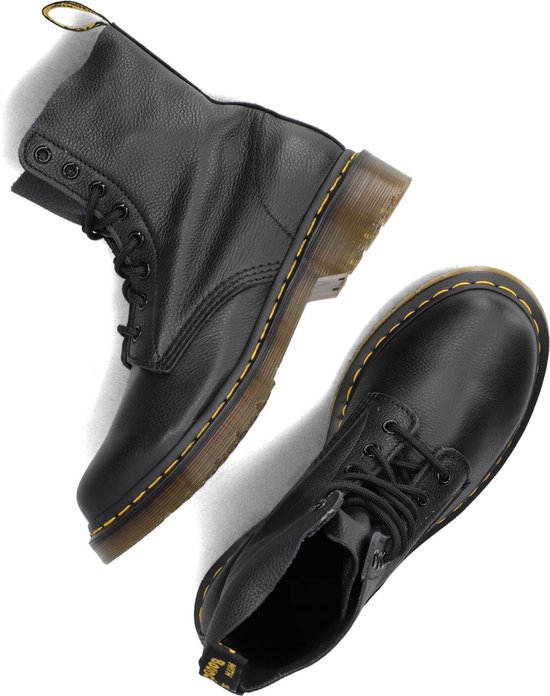 Paire de bottes Dr. Martens noires à lacets disposées de manière ludique, avec surpiqûre jaune.