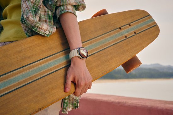 Een polshorloge met witte band met oranje en blauwe accenten, gedragen door een persoon die een longboard vasthoudt.