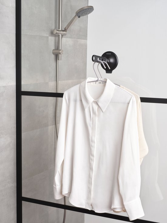 Zwarte inklapbare kledinghaak met zuignap, waarop een witte blouse en lichte jurk hangen.