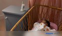 Babyfoon op nachtkastje naast een rieten wieg met slapende baby.