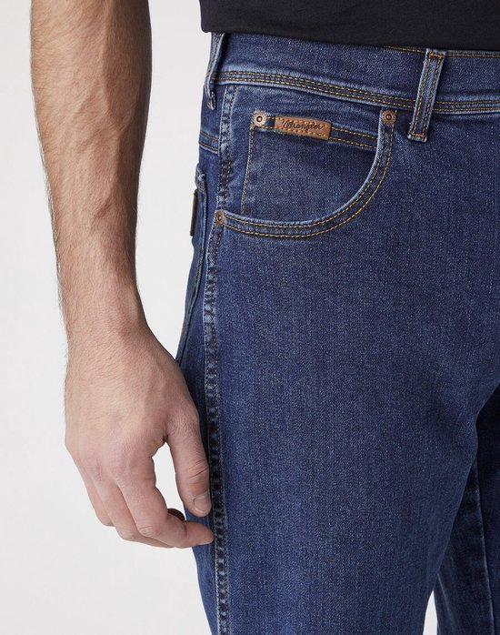 Sluiting van een spijkerblauwe Wrangler spijkerbroek met bruine naden en een bruin leren label.