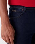 Detail van donkerblauwe Wrangler jeans: broekzak met bruin logo.