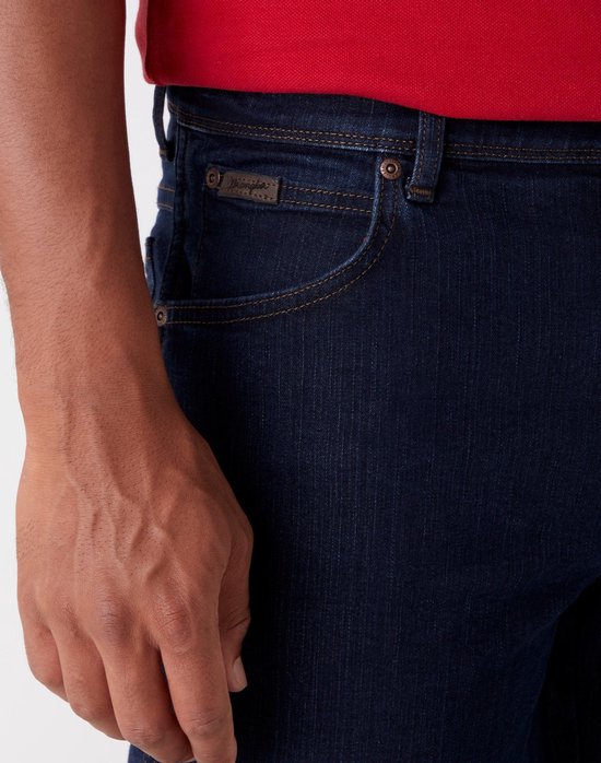 Detail van donkerblauwe Wrangler jeans: broekzak met bruin logo.