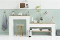 Briljant stalen Brabantia NewIcon prullenbak met zwart voetpedaal, onder een houten plank in een badkamer.