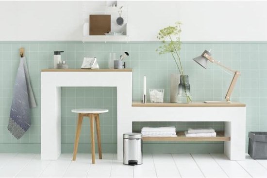Briljant stalen Brabantia NewIcon prullenbak met zwart voetpedaal, onder een houten plank in een badkamer.