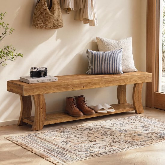 Houten halbank met bruine laarzen en witte slippers eronder. Twee kussens en een camera liggen op de bank.